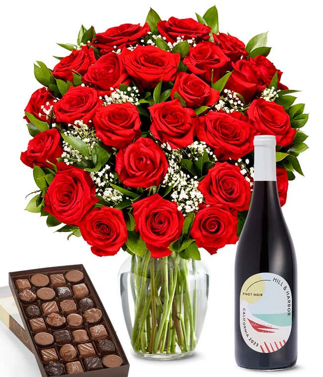A lush arrangement of 2 dozen red roses in a clear vase sits beside a bottle of Hill &amp; Harbor Pinot Noir and a 1-pound box of gourmet assorted chocolates.