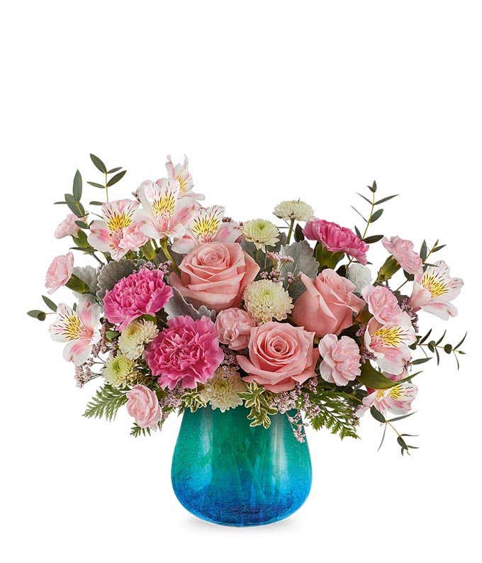 Pink roses, pink alstroemeria, pink carnations, white cushion poms, and floral greenery in a blue & green ombre glass vase