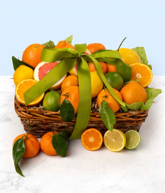 A basket brimming with fresh citrus fruits including oranges, grapefruits, lemons, and limes, decorated with a large green ribbon. 