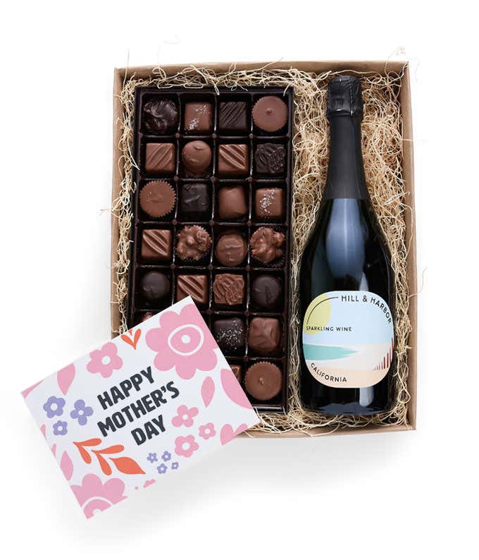A gift box with Hill & Harbor Sparkling wine and a 1 lb. box of assorted artisan chocolates with a 'Happy Mother's Day' card placed on top.
