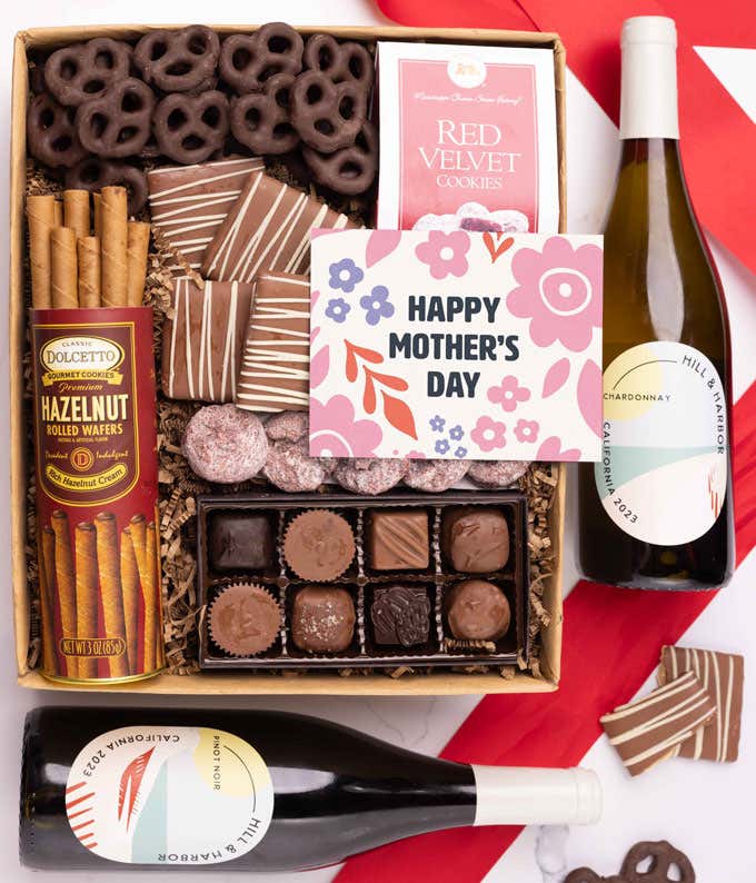 Bottles of Hill & Harbor Pinot Noir and Chardonnay paired with chocolate covered pretzels, mini chocolate chip cookies, a box of chocolates, and a 'Happy Mother's Day' card.