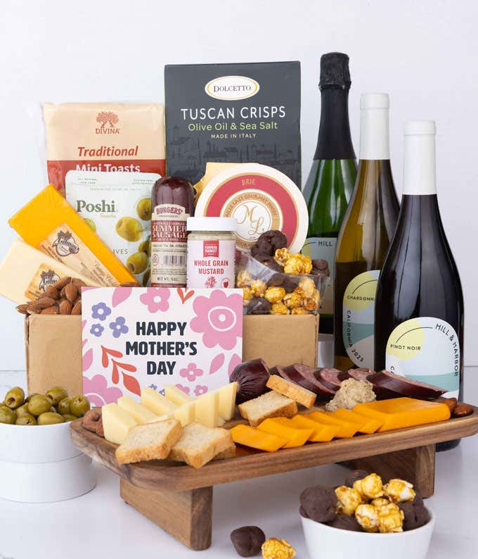A charcuterie spread with 3 cheeses, sausage, olives, crackers, mustard, almonds, and chocolate finished with bottles of red, white & sparkling wine and 'Happy Mother's Day' card.